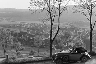 Zwei junge Frauen sitzen in einem Cabrio und blicken auf eine kleine Ortschaft im Schwarzwald