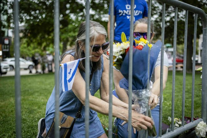 Zwei Frauen befestigen Blumen an einem Zaun in der Nähe des Tagtorts, eine der Frauen halt eine kleine israelische Flagge mit den Zähnen fest